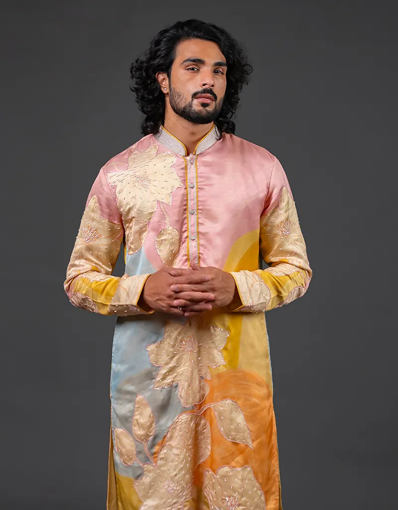 Man wearing a colorful traditional outfit with a gradient of pink, yellow, and blue on a dark background