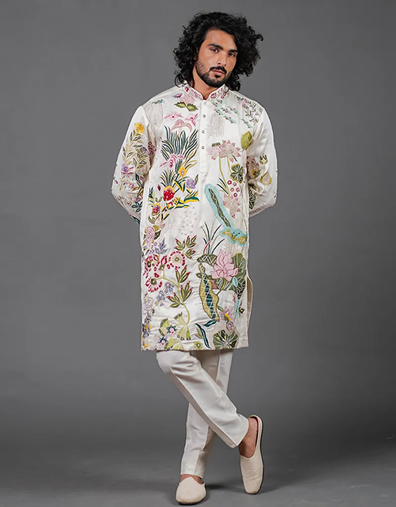 Man wearing a floral embroidered kurta with light-colored pants against a gray background