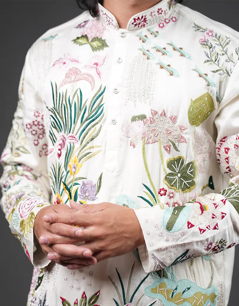 Person wearing a white embroidered traditional outfit with colorful floral patterns on a dark background