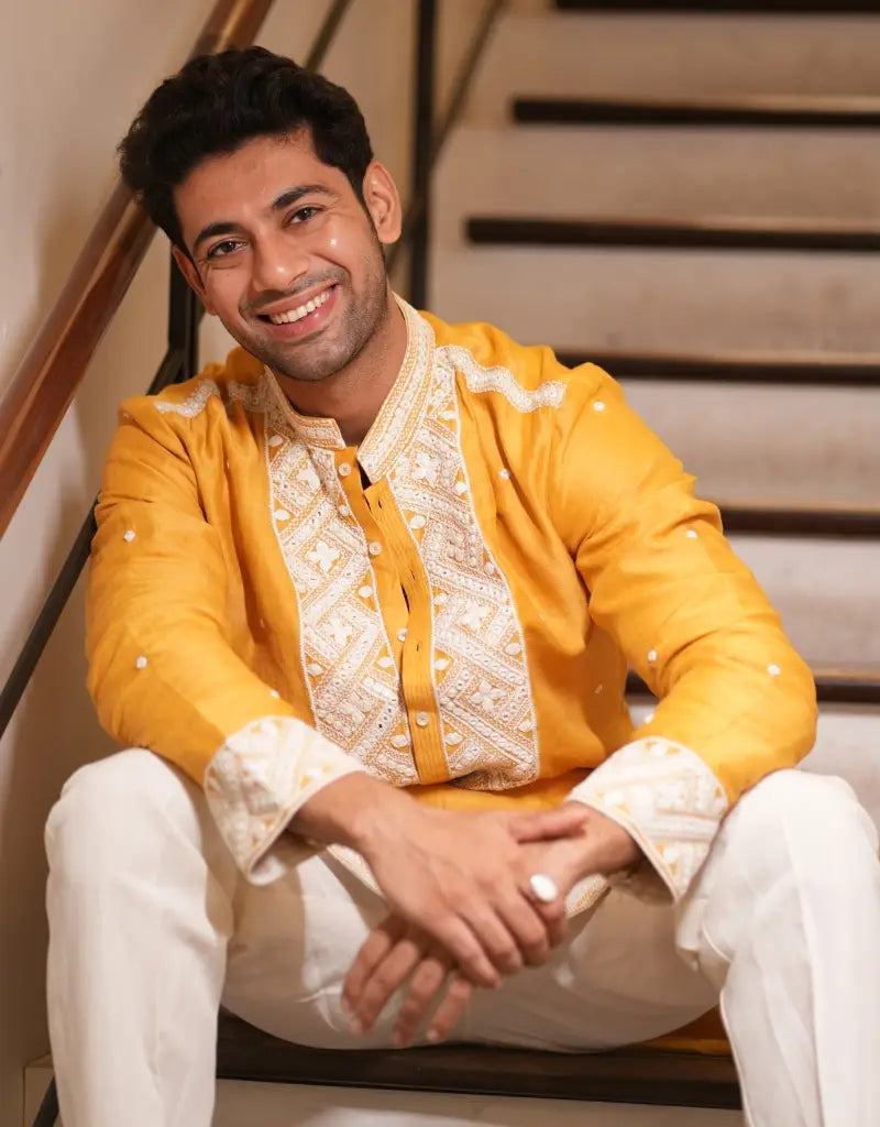Man wearing a yellow traditional Marigold Heritage Embroidered Kurta outfit sitting on stairs