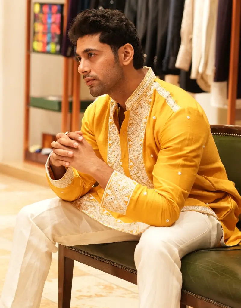 Man wearing a yellow embroidered kurta sitting on a chair in a clothing store.