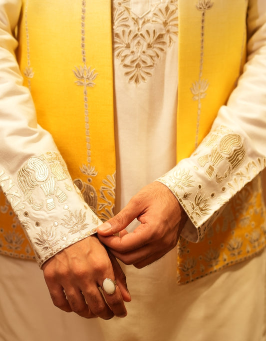 Close-up of hands holding each other wearing yellow and white embroidered traditional outfits.