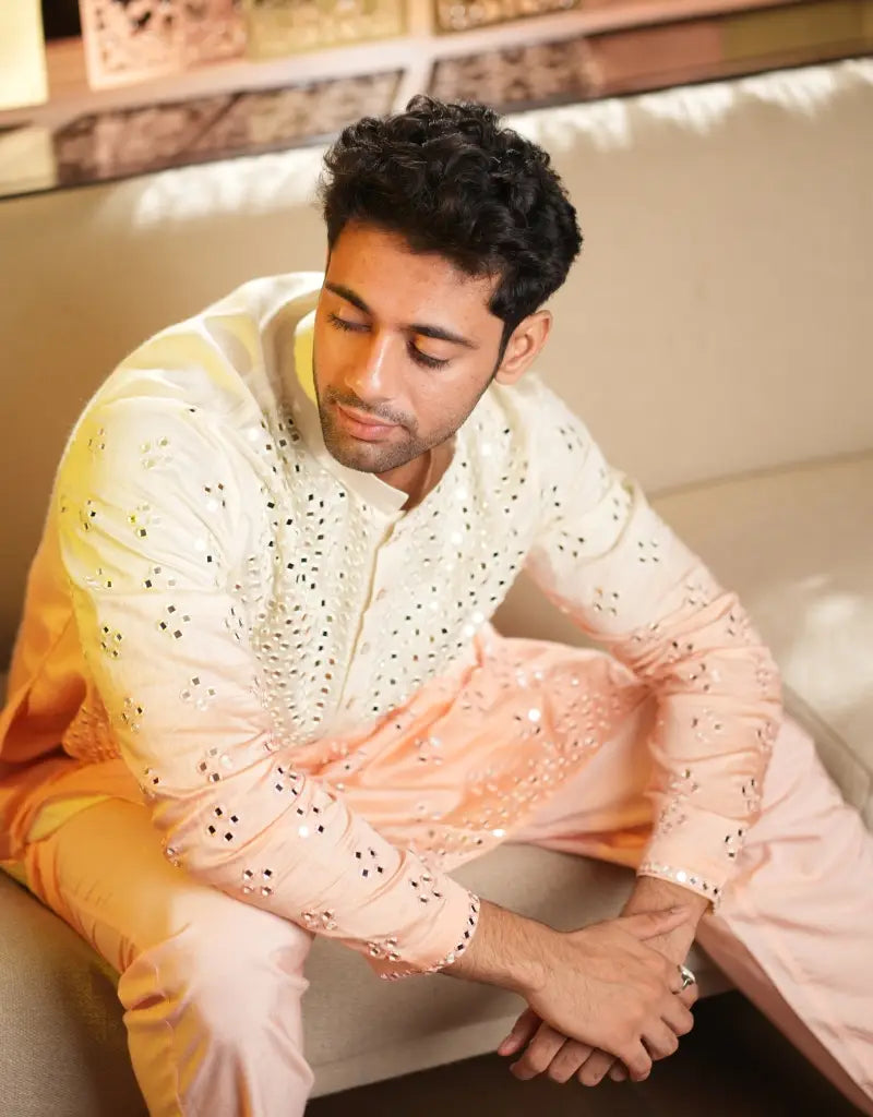 Man sitting on a couch wearing a traditional Blush Radiance Mirrorwork Kurta outfit with a blurred background