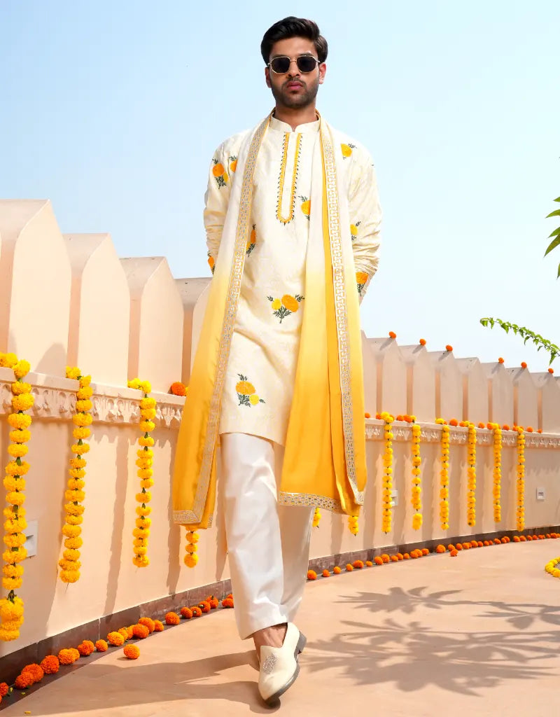 Man in traditional Marigold Work Kurta Set outfit with yellow and white dupatta against a decorated background