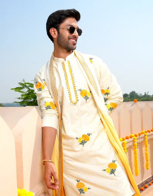 A man wearing a Marigold Work Kurta Set, a cream-colored traditional outfit with yellow floral patterns, outdoors.