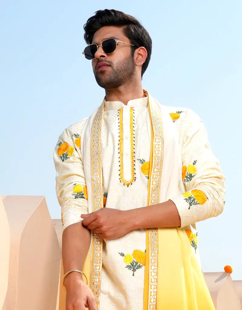 Man wearing a cream and yellow embroidered traditional Marigold Work Kurta Set outfit against a clear blue sky.