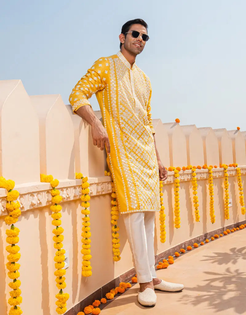 Man in a yellow kurta standing on a decorated balcony with yellow and orange decorations.