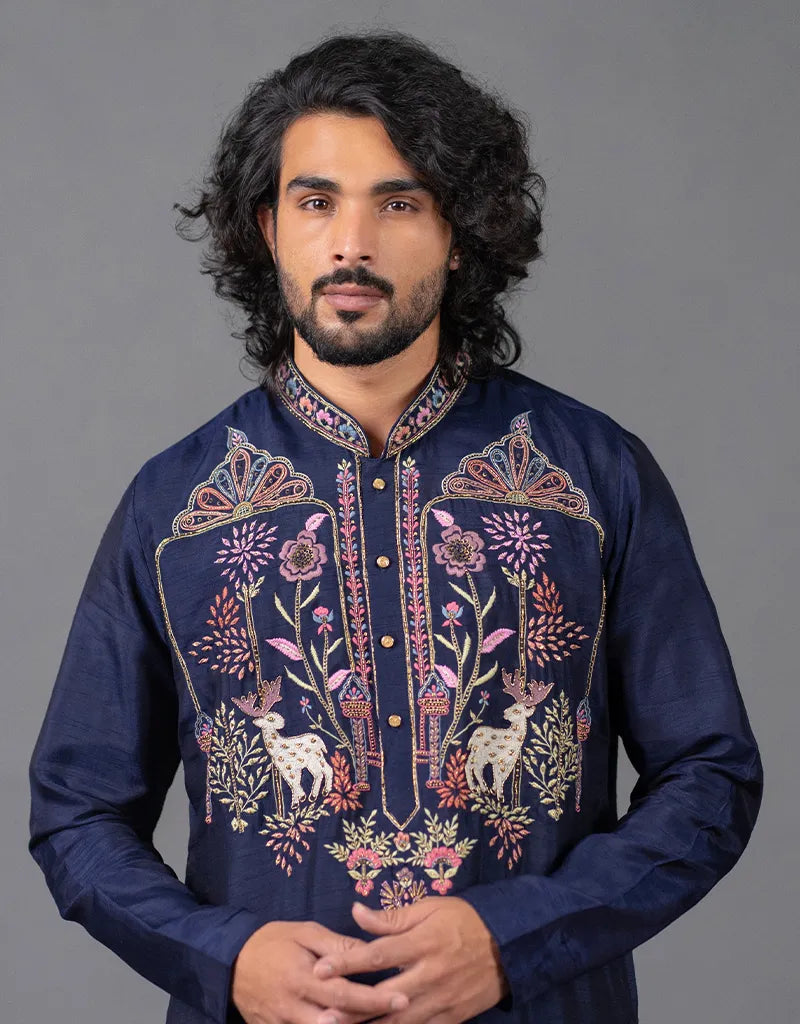 Man wearing a dark blue embroidered kurta against a gray background