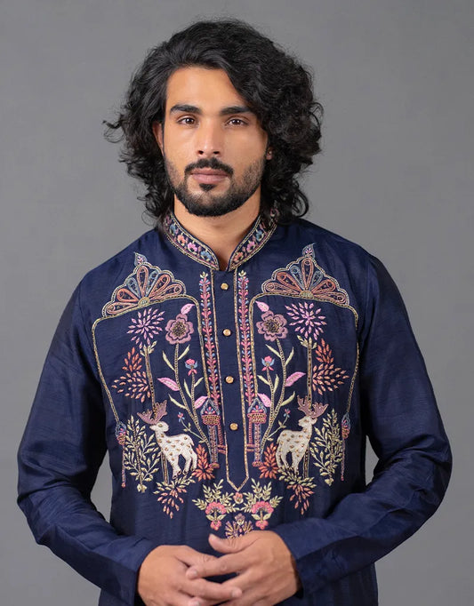 Man wearing a dark blue embroidered kurta against a gray background