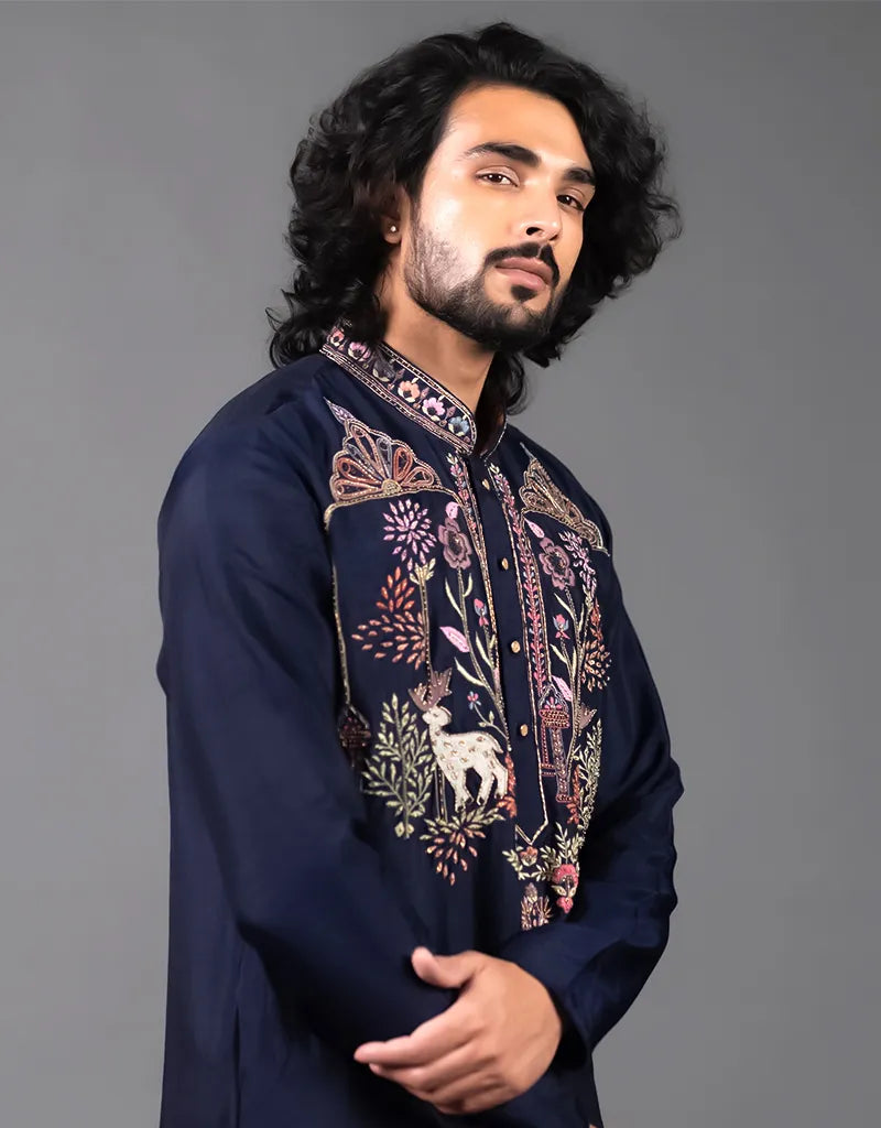 Man wearing a dark blue embroidered kurta against a gray background