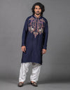 Man wearing a navy blue embroidered kurta with white pants on a gray background
