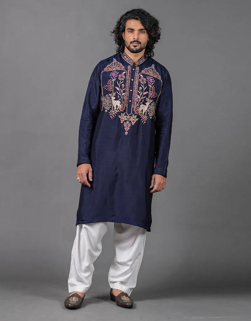 Man wearing a navy blue embroidered kurta with white pants on a gray background