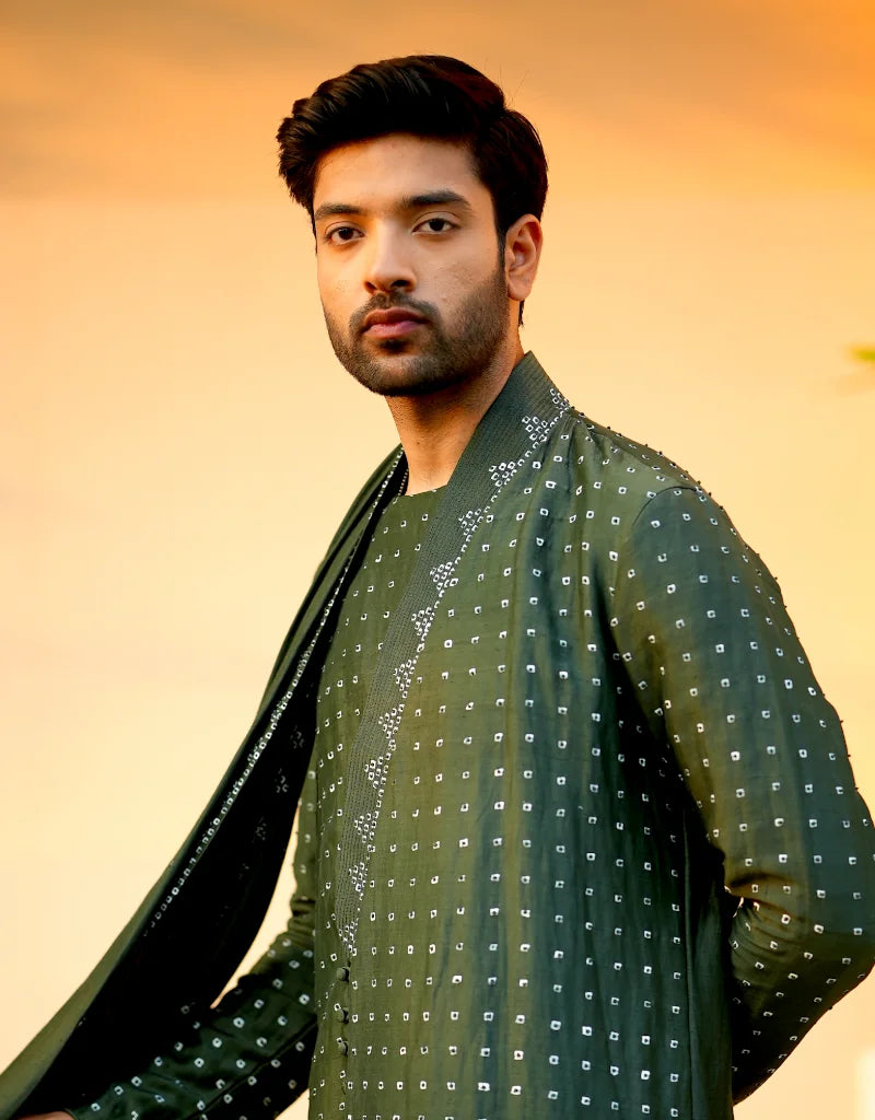 Man wearing a green traditional, verdant, elegant kurta set outfit with a patterned design against an orange background
