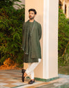 Man wearing a green kurta with white pants standing outdoors near a column.