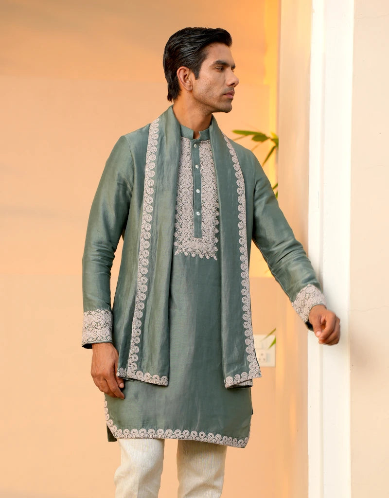 Man wearing a traditional green kurta with white embroidery against a peach background