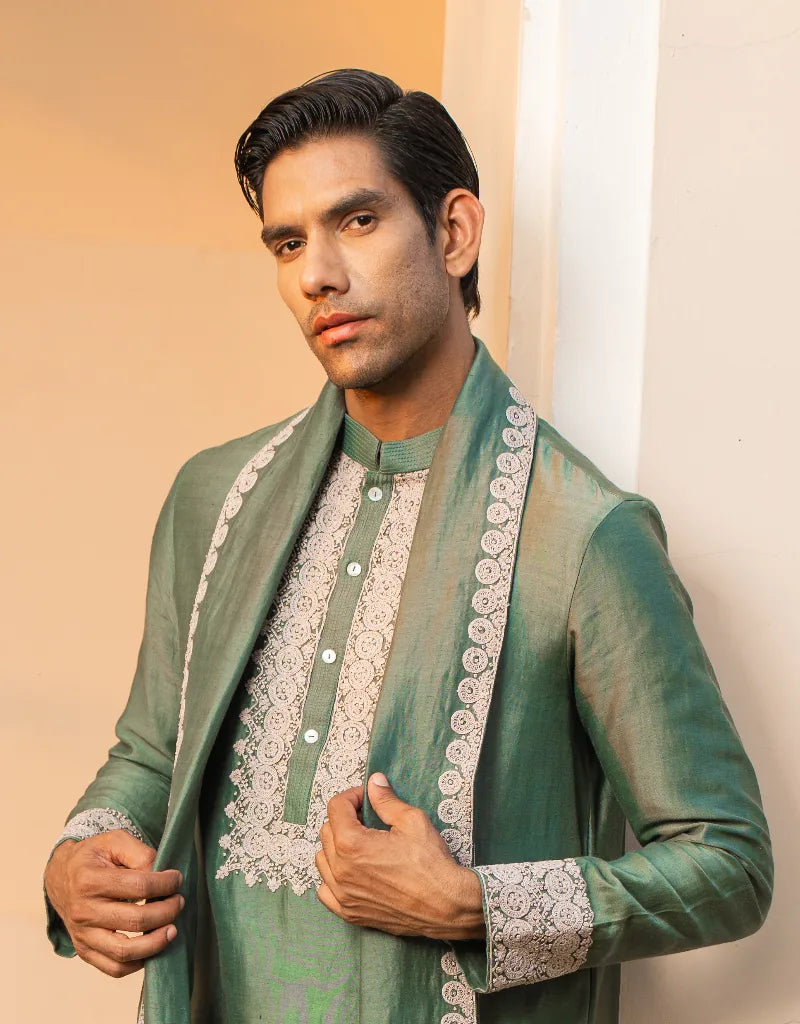 Man wearing a green traditional outfit with white embroidery against a beige background
