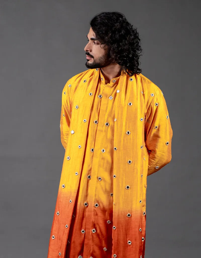 Man wearing a yellow and orange traditional outfit with decorative patterns on a gray background