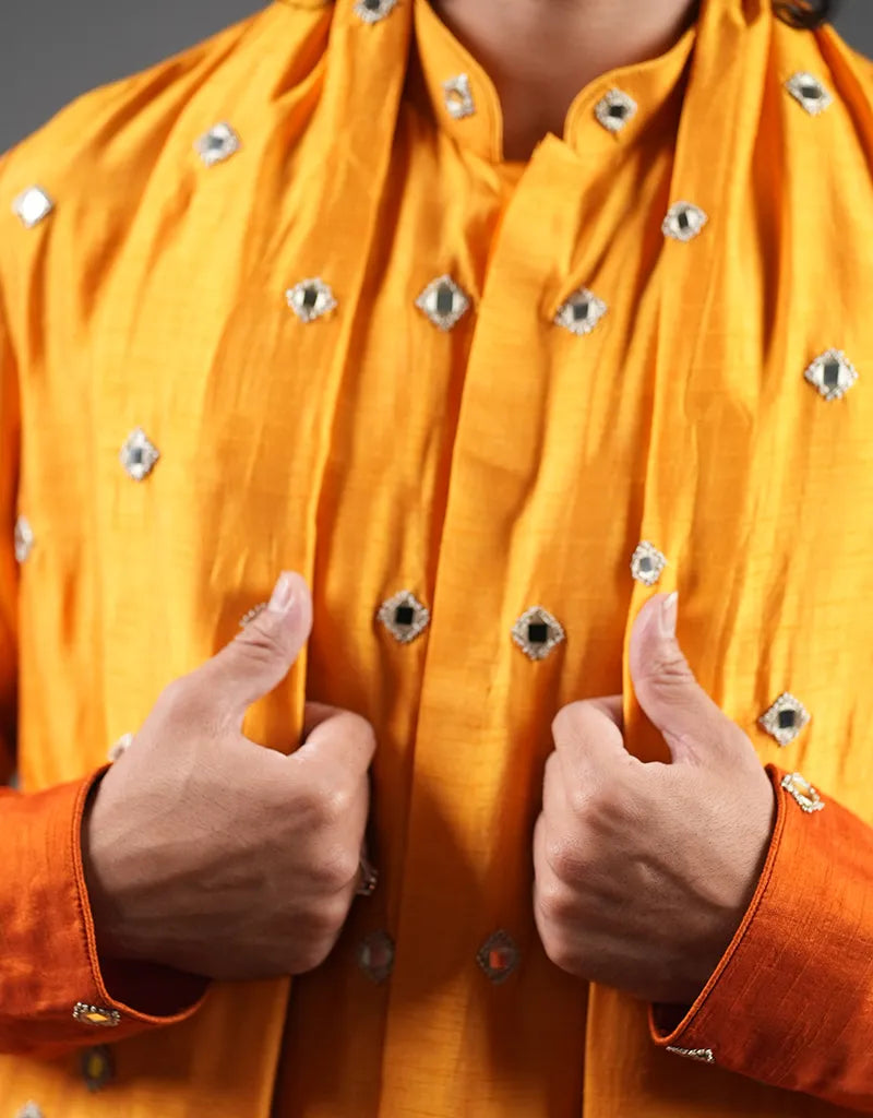 Person wearing an orange traditional kurta outfit with decorative buttons, giving a thumbs-up gesture.