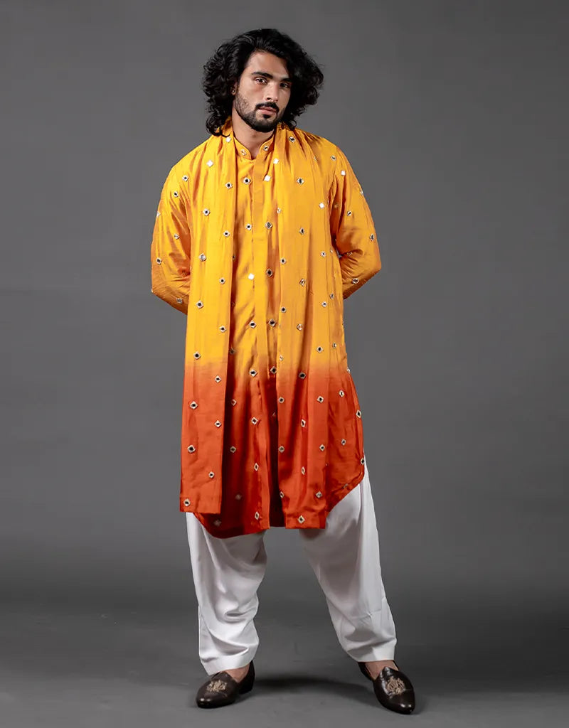 Man wearing a yellow to orange gradient kurta with white pants on a gray background