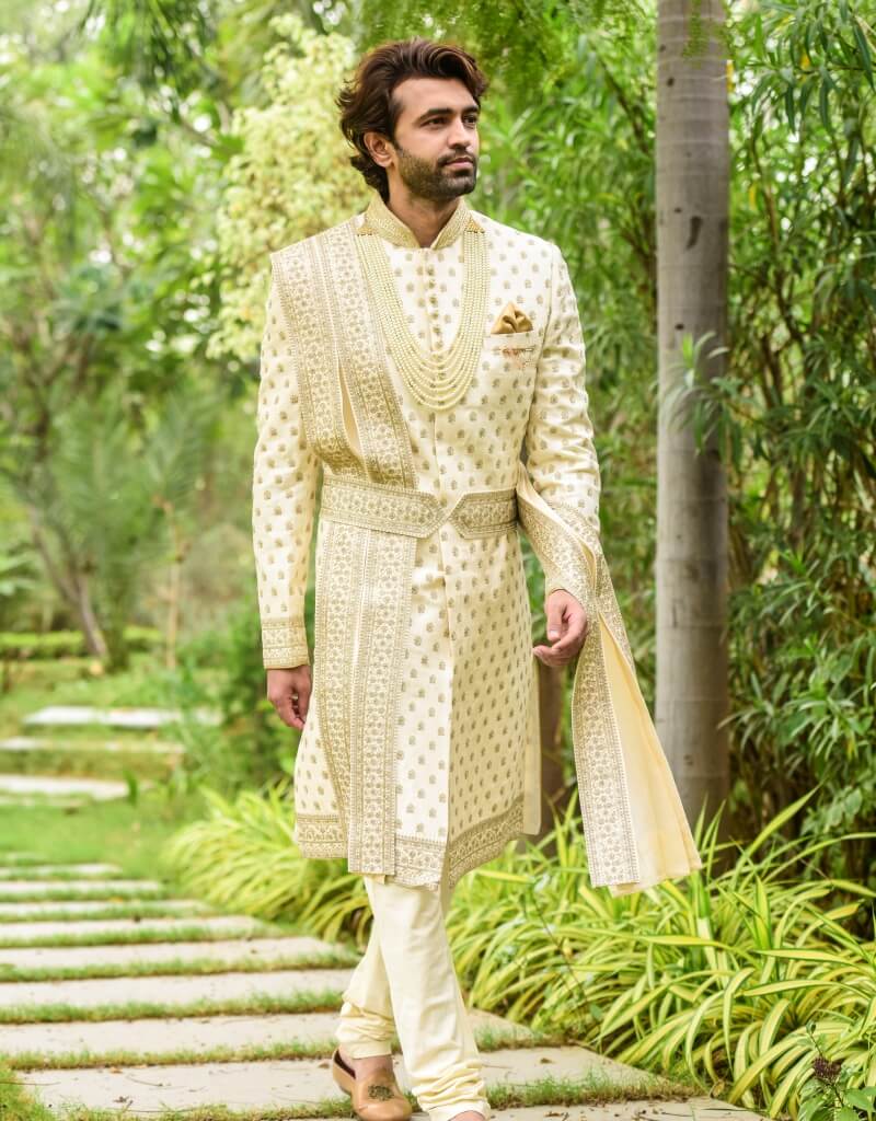 A man wearing a four-piece sherwani in raw silk with gold inlay boota work—cream from The HUB.