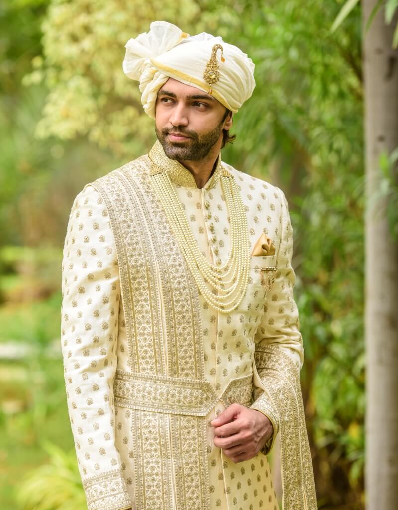 A man wearing a four-piece sherwani in raw silk with gold inlay boota work—cream from The HUB.