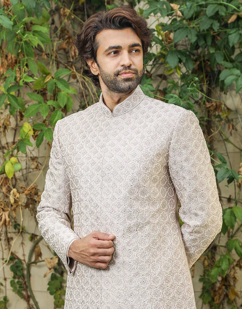 A man wearing a three-piece sherwani in satin silk with resham & pearls in onion pink from The HUB.