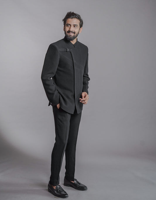 A man wearing two-piece Jodhpuri suit of netted, stretched fabric in black from The HUB.