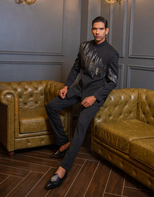 A man in a stylish classic Bandhgala Indo-Western outfit sitting on a green leather couch in an elegant room.