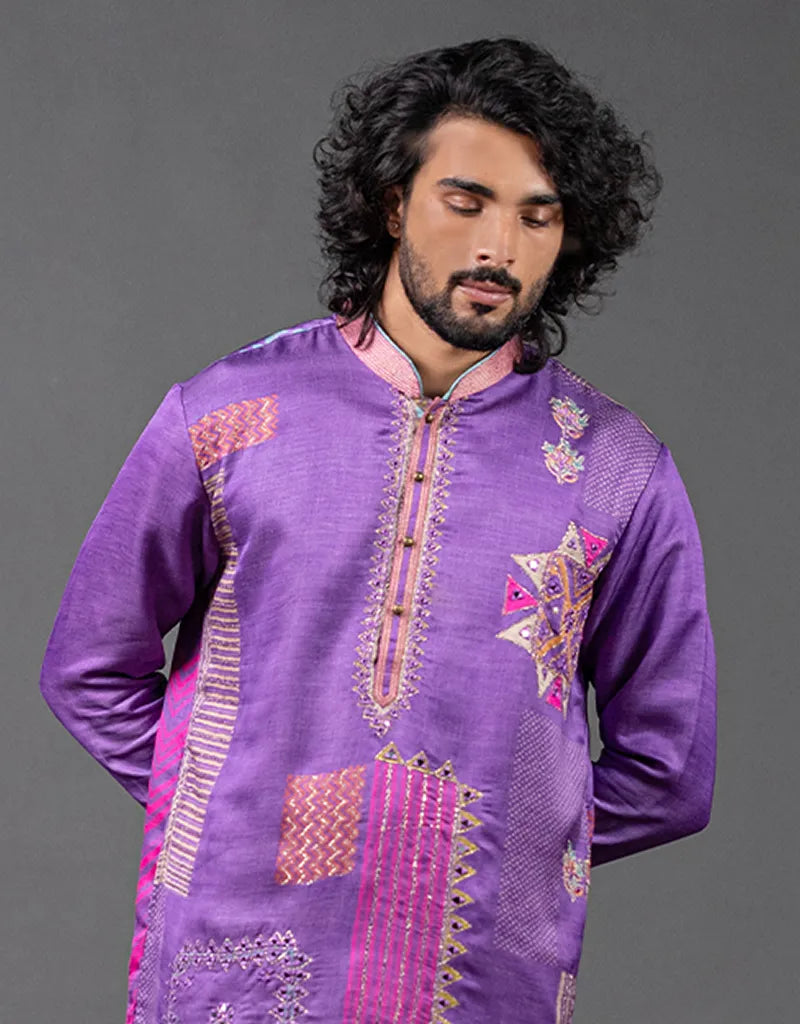 Man wearing a purple embroidered traditional outfit against a gray background